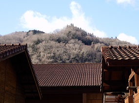 体験小屋の屋根の合間から除く近くの山の風景。
